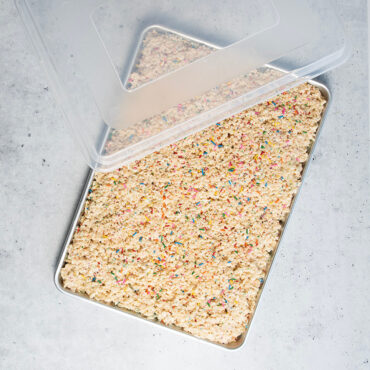 Nordic Ware aluminum big sheet pan with clear storage lid, filled with golden rice crispy treats