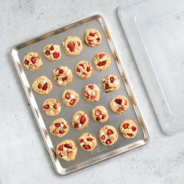 Nordic Ware aluminum big sheet pan with clear lid, containing golden baked cookies arranged on surface