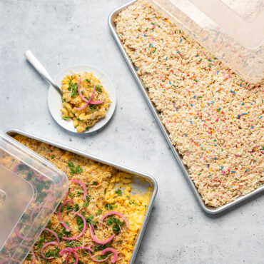 Nordic Ware aluminum sheet pans with clear plastic storage lids, containing baked mac and cheese and rice crispy treats