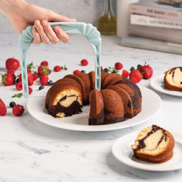 Nordic Ware bundt slicer cutting through golden bundt cake, showing clean even slices being made