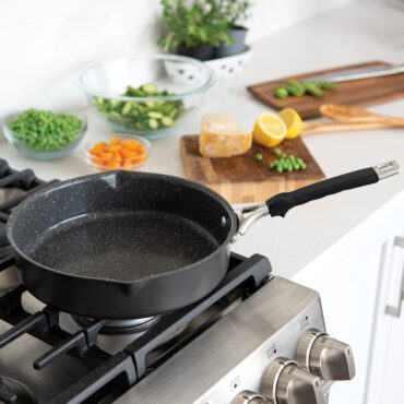 Nordic Ware Verde 10-inch ceramic nonstick skillet with lid on stovetop, green exterior, raw vegetables nearby