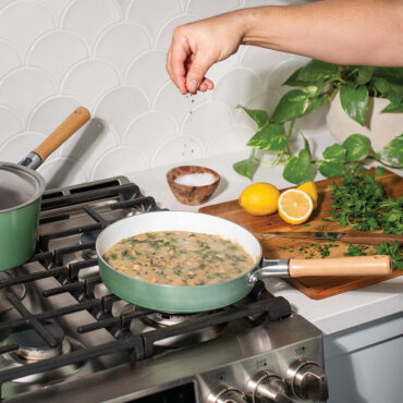 Nordic Ware cardamom ceramic nonstick 10-inch skillet on stovetop with creamy pasta being garnished by hand