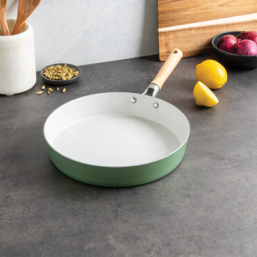 Nordic Ware cardamom ceramic nonstick 12-inch skillet with golden interior, surrounded by fresh herbs and cooking utensils