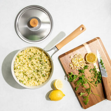 Nordic Ware 3-quart aluminum saucepan with lid beside it, filled with white rice, lemons and cutting board nearby