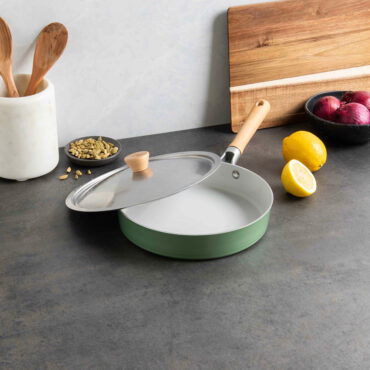 Nordic Ware Cardamom 10-inch nonstick frying pan with glass lid, dark exterior, styled with cooking ingredients
