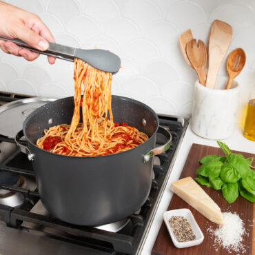 8qt Stock Pot with Lid on stovetop with spaghetti; hand using tongs to pull some pasta from pot