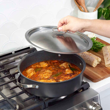 Nordic Ware Verde braiser pan with lid on stovetop, containing simmering chicken and vegetable stew