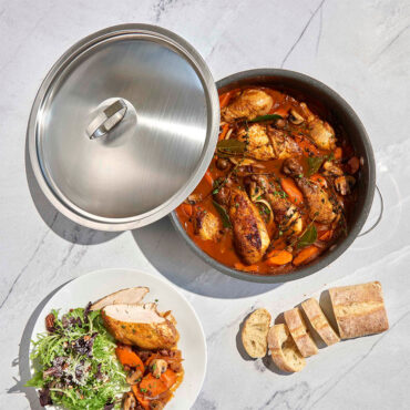 Nordic Ware Verde green braiser pan with lid beside plated chicken stew, vegetables, and sliced bread