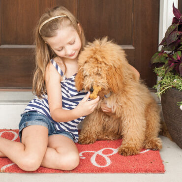 Young girl on outdoor steps feeding homemade bone-shaped dog treats to golden puppy from Nordic Ware treat pan