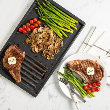 Nordic Ware basalt dual-zone grill griddle with seared steak, grilled vegetables, and plated meal on countertop