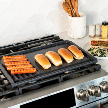 Nordic Ware black cast aluminum dual-zone grill griddle on stovetop cooking hotdogs and toasting buns