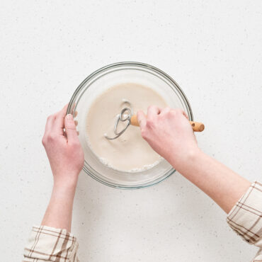 Nordic Ware Danish whisk mixing sourdough dough in clear glass bowl, hands kneading sticky bread mixture