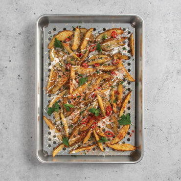 Nordic Ware aluminum half sheet pan with wire cooling rack, filled with golden roasted potato wedges