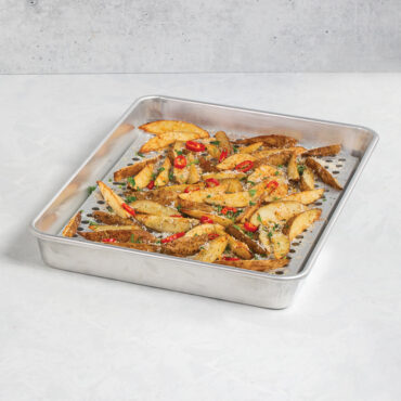 Nordic Ware aluminum half sheet pan with wire cooling rack, filled with golden roasted potato wedges