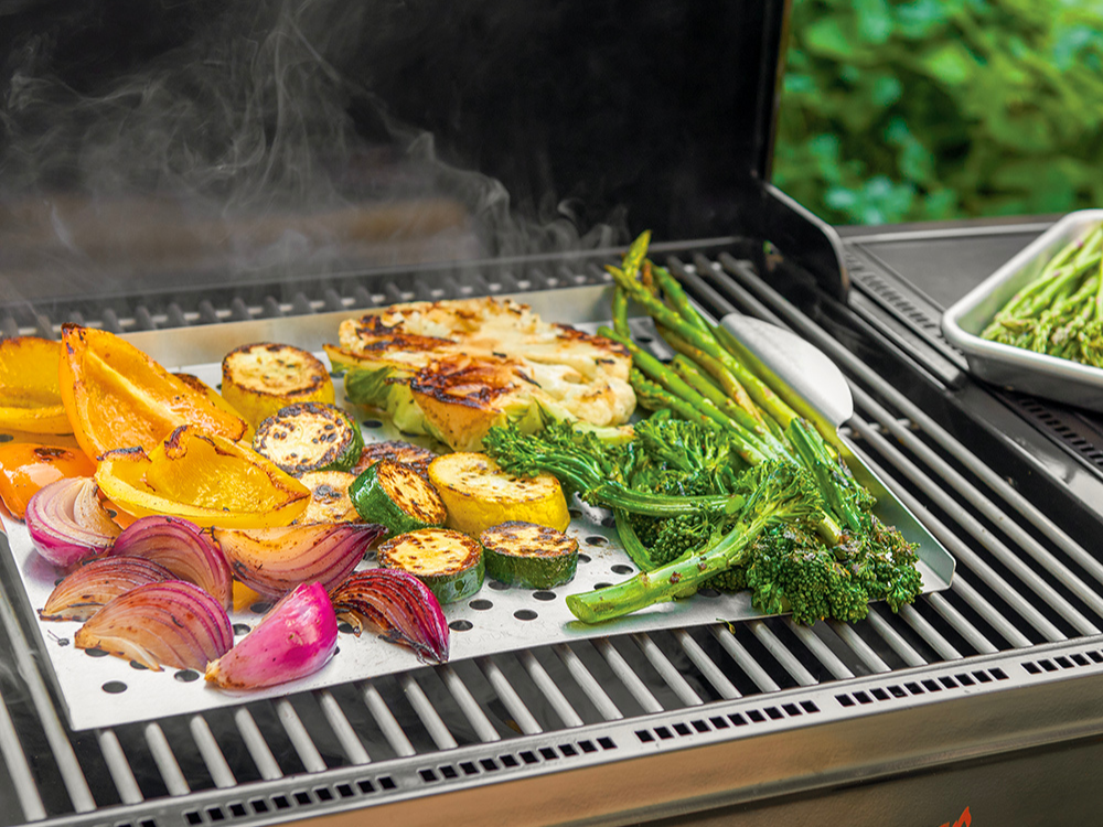 Perforated Grill Topper on a grill cooking vegetables including broccoli, cauliflower, zucchini, bell peppers, and onions.