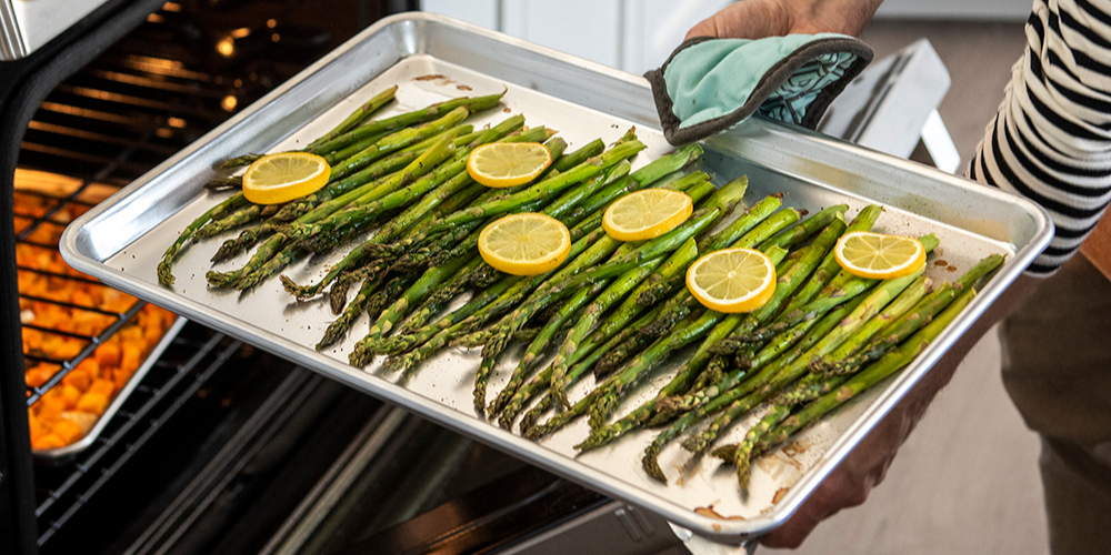 Roasted asparagus coming out of the oven on a baker's half sheet pan.