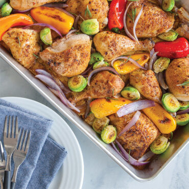 Roasted golden chicken with vegetables in Nordic Ware aluminum high-sided sheet pan, served portion plated beside