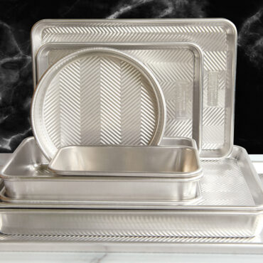 Nordic Ware Prism black non-stick baking pans with lid stacked on white marble surface