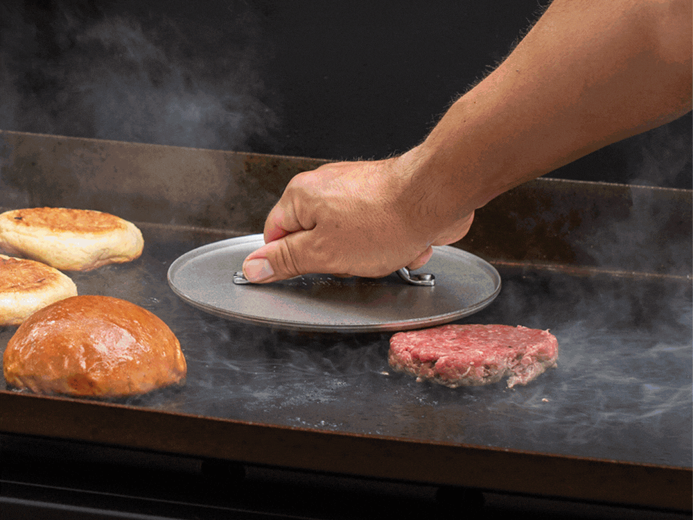 Gif of three images showing off the grilling burger set. The first image features the Heavyweight Grill Press making smash burgers on a Blackstone Grill. The second features the High Dome Grill Lid melting cheese on the smash burgers on the Blackstone Grill. The third features the smash burgers served on a 2 Pack of Burger Serving Trays with watermelon and elote corn salad.