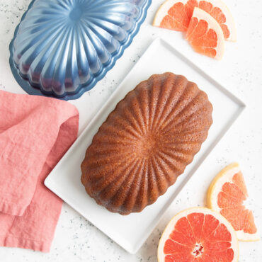 Sliced vanilla pound cake on white plate with Nordic Ware aluminum fluted loaf pan and orange garnish