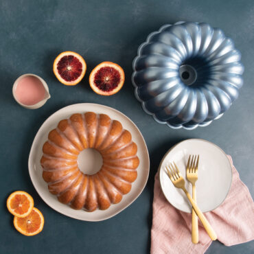 Glazed bundt cake from Nordic Ware Formed Elegant Party pan with orange slices, golden forks on white plates