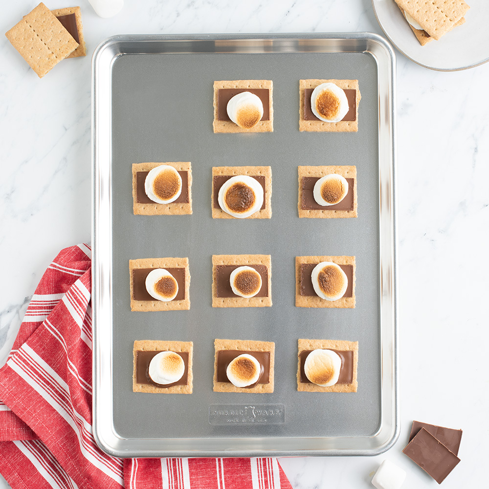 Baked and toasted smores on a baking sheet ready to be topped with an additional graham cracker and served.