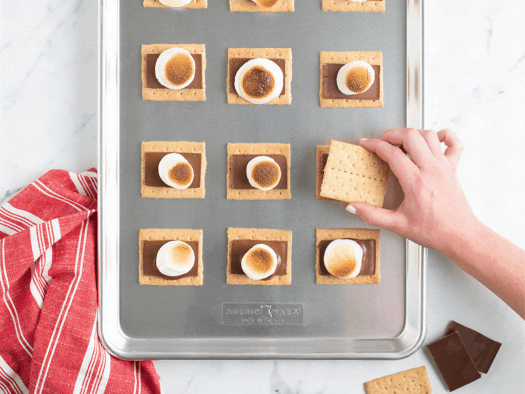 Gif of a hand adding a graham cracker to the top of a baked and toasted smore on a baking sheet.