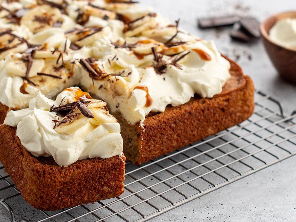 Up close image of sliced cake topped with a whipped cream frosting on a baking sheet.