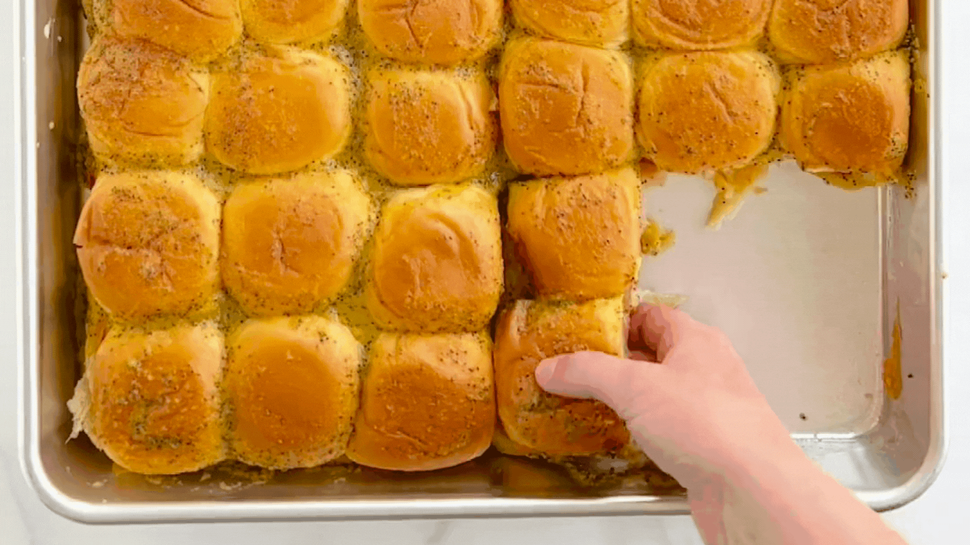 Hand pulling a baked ham and cheese slider out of a Naturals® Big Batch Pan.