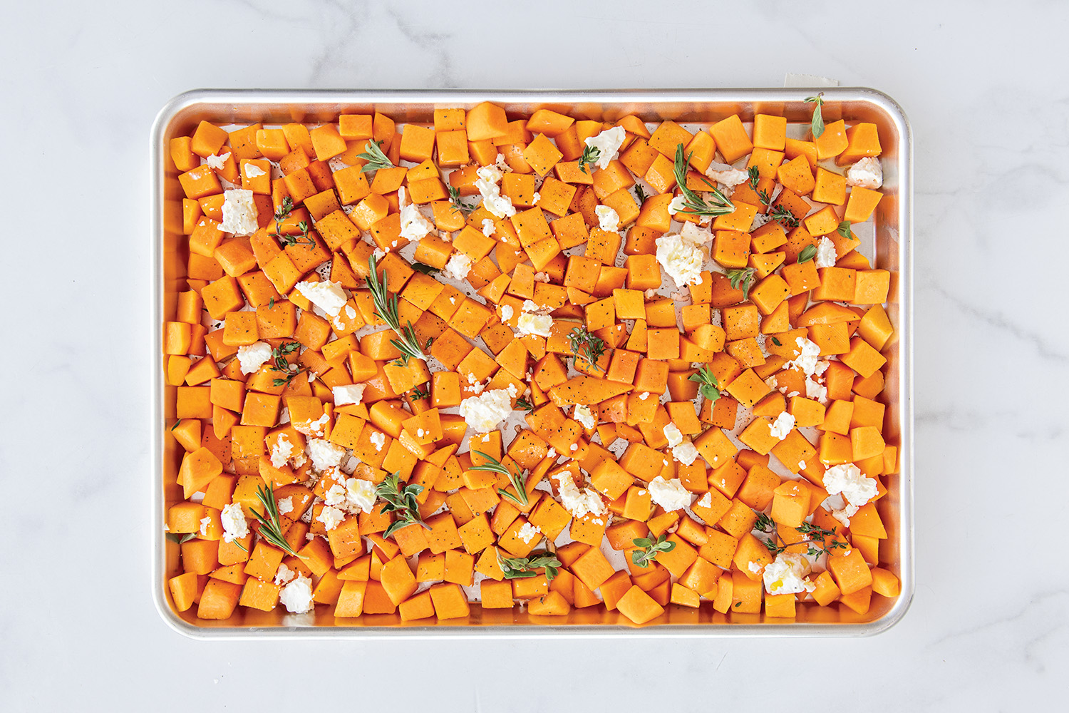 Cubed butternut squash on a Naturals Half Sheet Pan topped with cheese and herbs. 