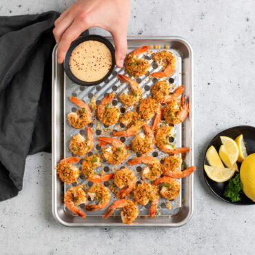 Overhead image of  Quarter Sheet & Multi Task Rack with shrimp, hand placing sauce on rack, sliced lemons next to pan