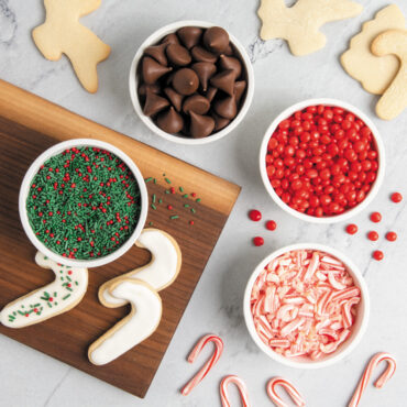 Four white mini bowls arranged on white countertop with crushed candy cane, red and green sprinkles, and red candies