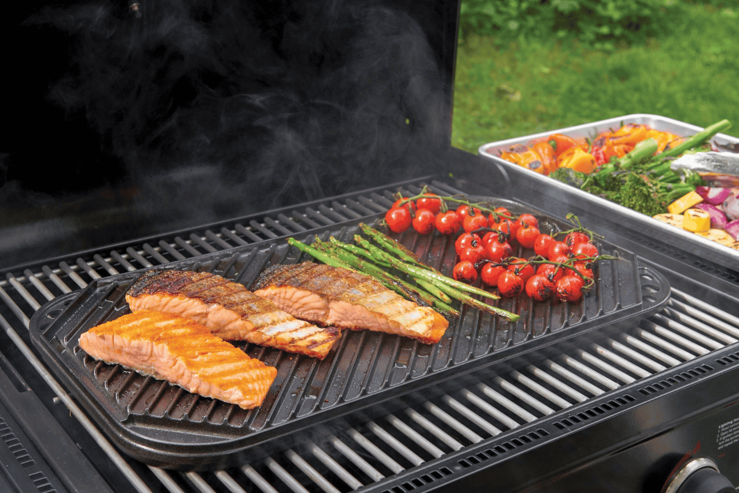 Gif of Two Burner Reversible Griddle on grill cooking vegetables on the smooth side and salmon on the ribbed side.