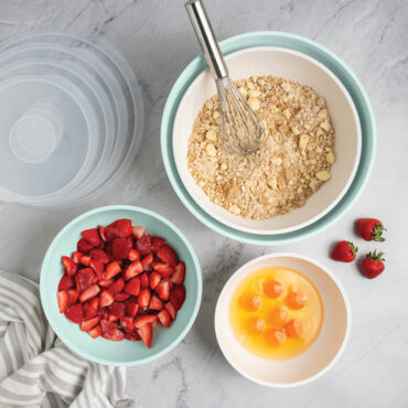 overhead of Nordic Ware 8 piece seaglass and white 7 quart, 5 quart, 3.5 quart and 2 quart bowls filled with dough, strawberries, and egg yolks