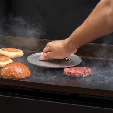 hand pressing burger patties on grill with nordic ware weighted grill press