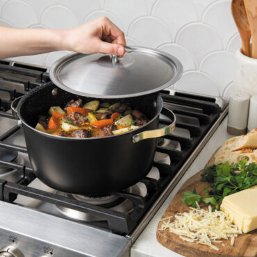 nordic ware 6 qt aluminum dutch oven on stovetop with stew; hand lifting lid by the knob