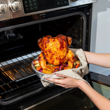 roasted chicken on vertical chicken roaster being taken out of oven