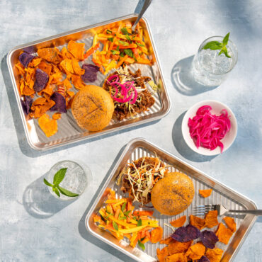 Two Nordic Ware aluminum prep trays holding grilled burgers, golden fries and chips in outdoor BBQ setting