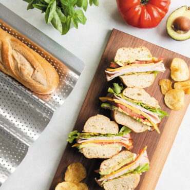 baguette sandwich cut into four pieces on cutting board with loaf nested in Nordic Ware baguette & french bread pan