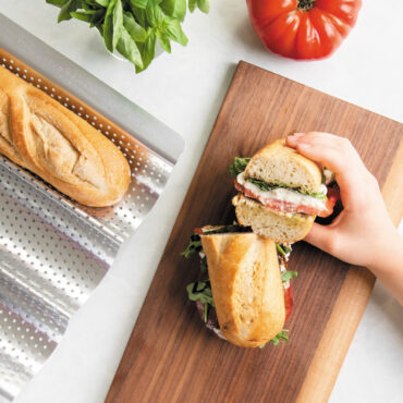 hand holding up half of baguette sandwich on cutting board with loaf nested in Nordic Ware baguette & french bread pan