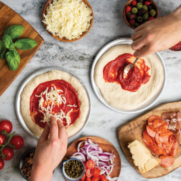 hands applying pizza ingredients to dough on hot air pizza crispers