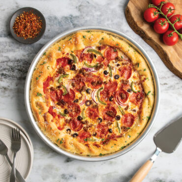 nordic ware 14 inch deep dish pizza pan with supreme pizza next to cake server with wooden handle