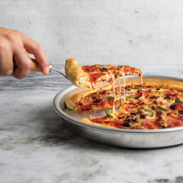 hand using server to lift a slice of pizza from deep dish pizza pan