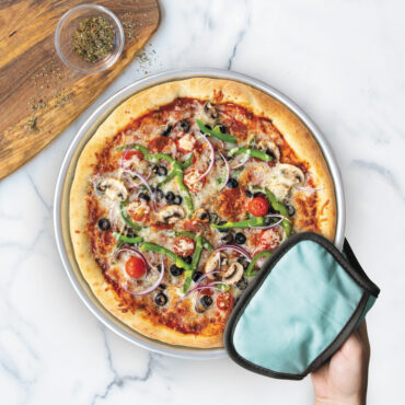 hand using hot pad to hold pizza pan with supreme pizza