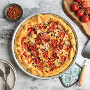 nordic ware deep dish pizza pan with supreme style pizza next to cake server and hot pad