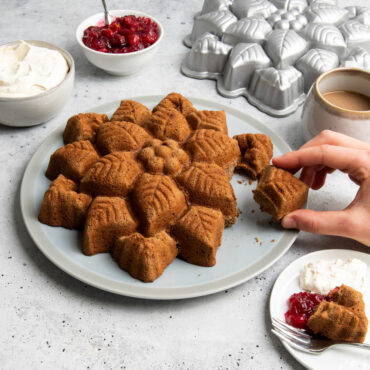 nordic ware cast aluminum poinsettia pull apart pan and plated cake on countertop with silverware and warm beverages; hand pulling off a piece of cake